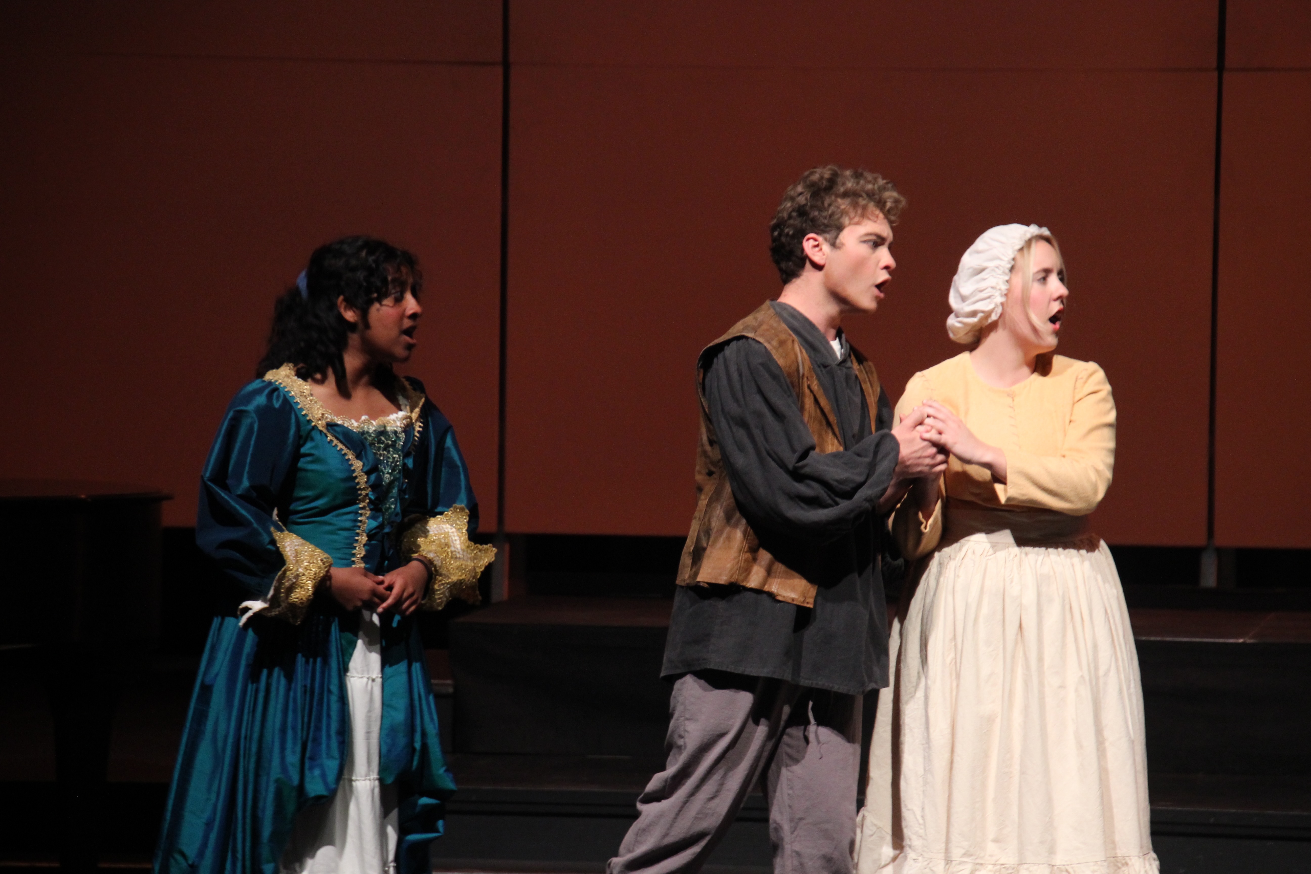 Photo Declan Galli, Center wearing leather vest, black blouse, grey pants. Left Woman wearing blue dress, right woman wearing light yellow dress.